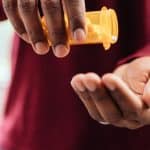 man in red shirt pouring pills from prescription pill bottle