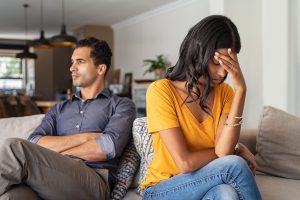 A couple sitting on the sofa turned away from each other after having an argument about addiction.